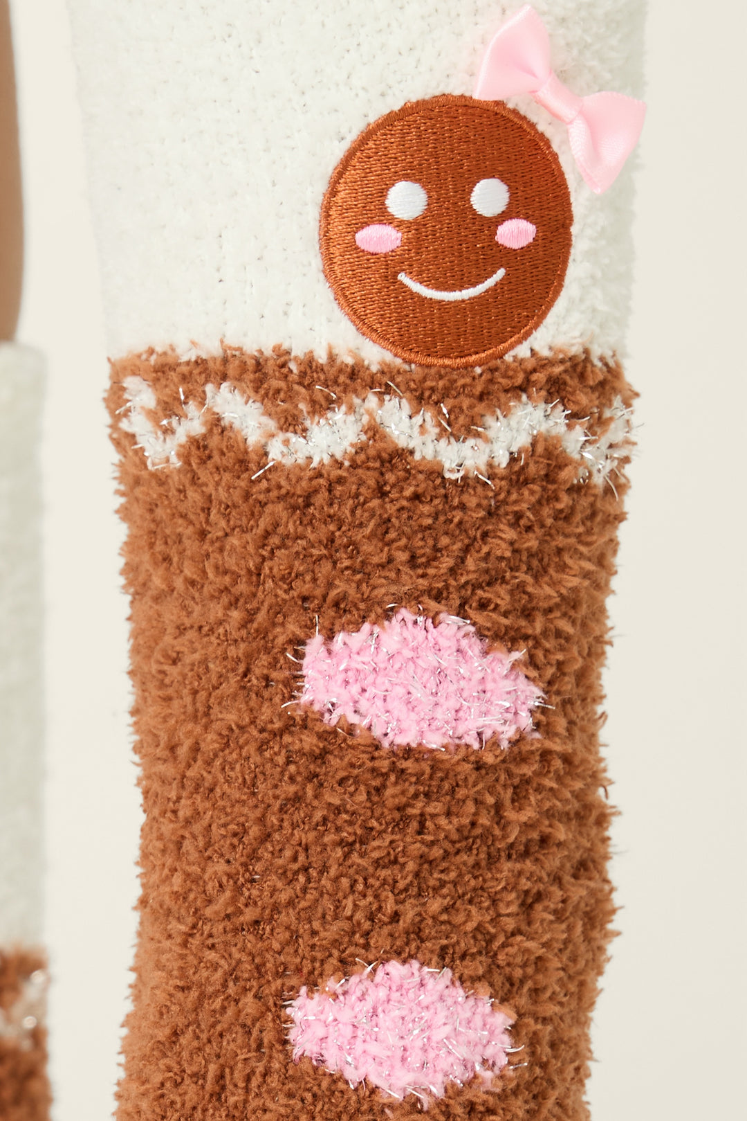 A close-up of P.J. Salvage Ski Jammie Classics Gingerbread Man Crew Socks with grippers, featuring a brown base, white trim, pink details, and a patch of a smiling gingerbread face decorated with a pink bow.