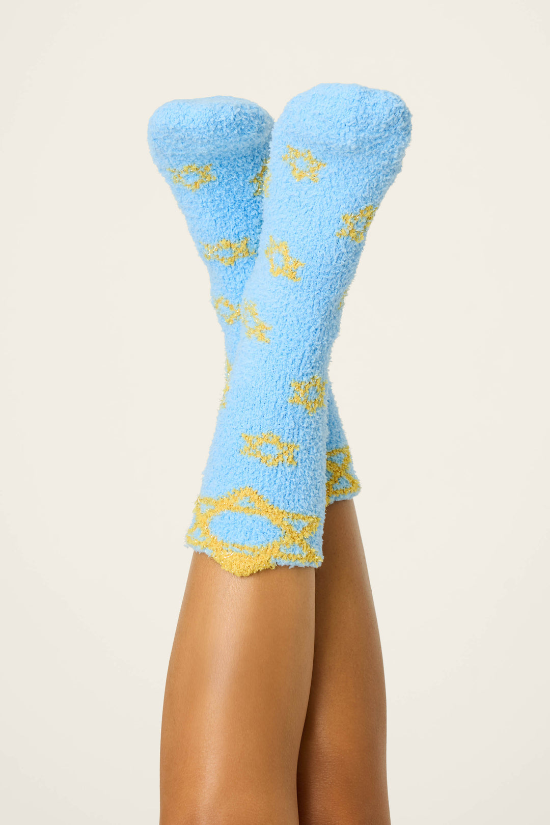 A pair of legs in the air showcases fuzzy light blue STARS SOCKS with yellow Star of David patterns from the P.J. Salvage BOYFRIEND BOXER SHORT GIFT SET, set against a plain, light background.