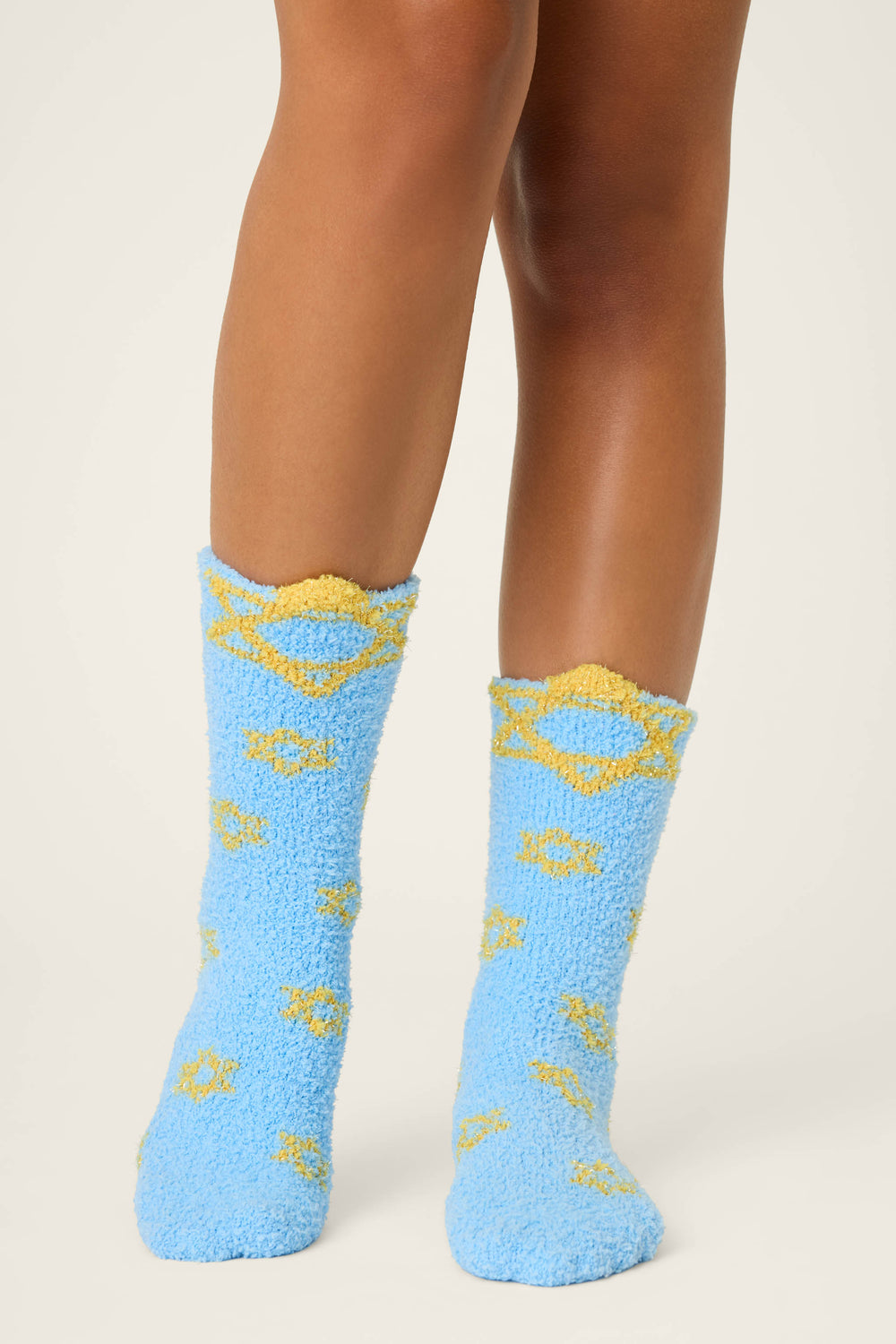 A person stands on an off-white background wearing P.J. Salvage STARS SOCKS BOYFRIEND BOXER SHORT GIFT SET blue fuzzy socks featuring yellow Star of David designs.