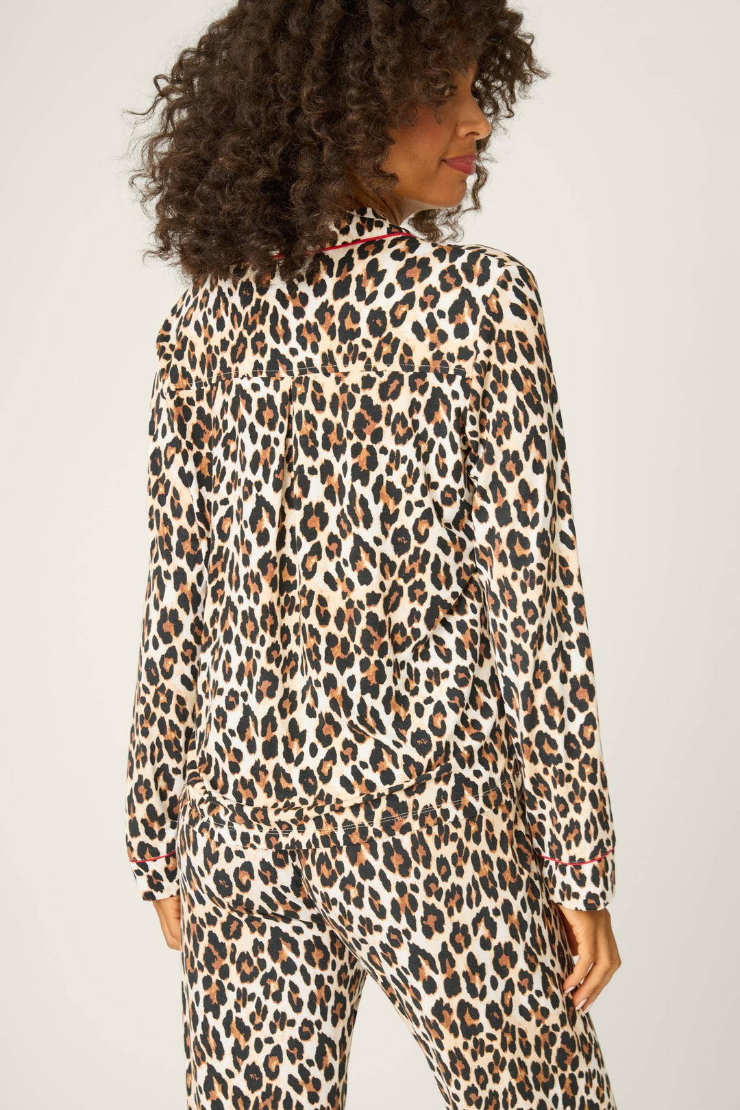 A person with curly hair is seen from behind wearing the P.J. Salvage Holiday Dreams Leopard Print Long Sleeve Top, paired with matching pants, against a plain light background.