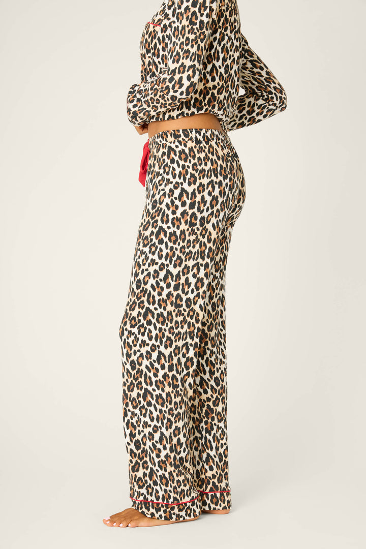 A person stands barefoot in profile against a plain light background, wearing P.J. Salvage's Holiday Dreams Leopard Print Open Leg Pants, featuring a long-sleeve top, loose fit pants, and a red waist drawstring.