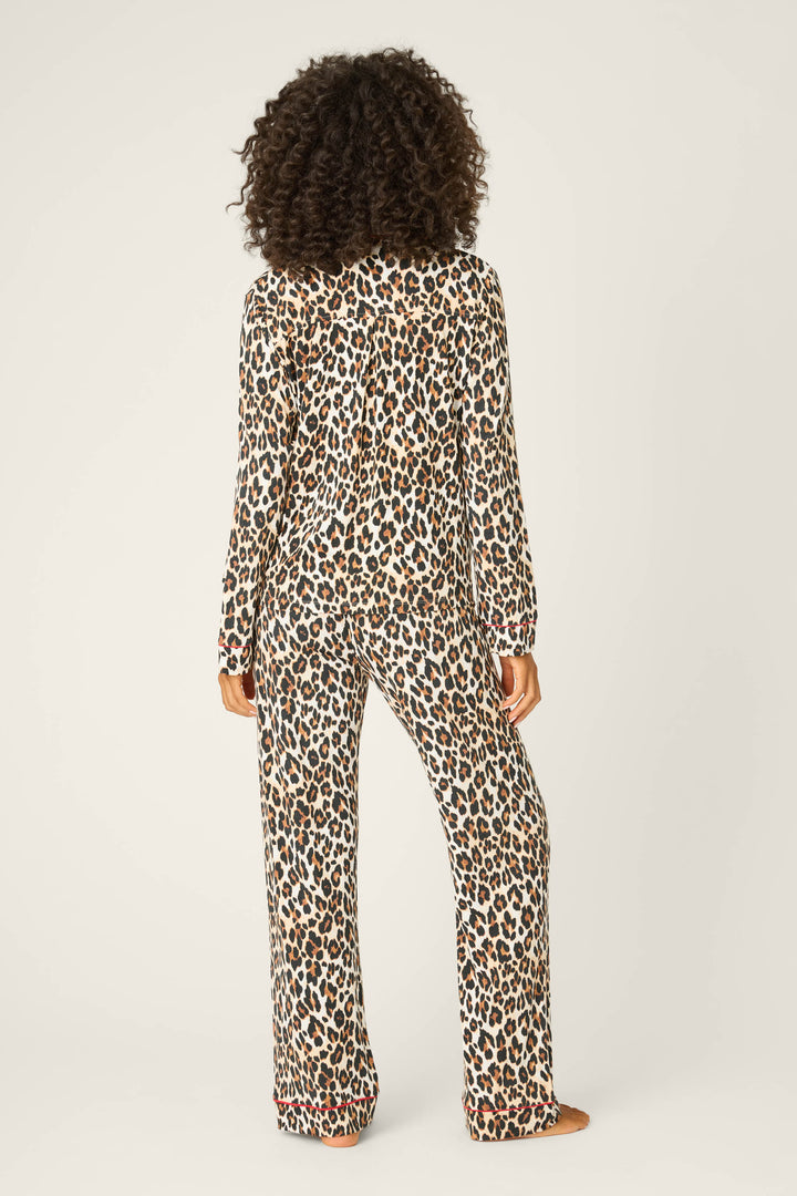 A person stands barefoot, facing away, wearing the P.J. Salvage LEOPARD PJ SET HOLIDAY DREA—a matching long-sleeve top and pants with an all-over leopard print—against a plain, light background.