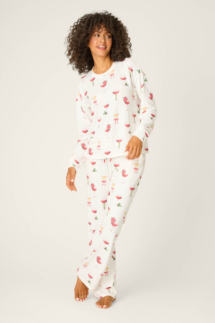 A person with curly hair wears the P.J. Salvage Let's Get Toasty Holiday Wine Print Long Sleeve Top, standing barefoot against a plain light background.