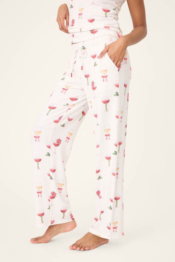 A person stands barefoot in P.J. Salvage's Let's Get Toasty Holiday Wine Print Open Leg Pants, featuring a drawstring waist and colorful wine glass prints, with one hand in a pocket and the other near their waist.
