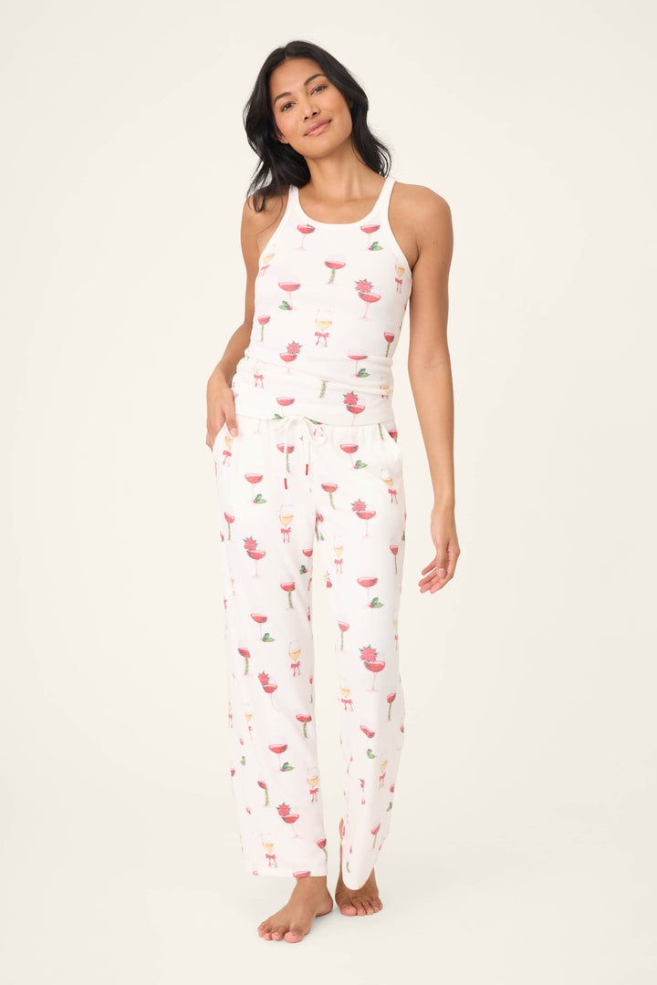 A woman stands barefoot against a light background, wearing P.J. Salvage's Let's Get Toasty Holiday Wine Print Open Leg Pants and a white sleeveless tank top.