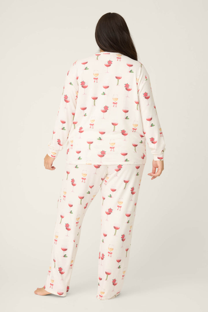 A person with long dark hair stands barefoot, facing away, wearing the P.J. Salvage Let's Get Toasty Holiday Wine Print Plus Size Pants Set against a plain light background.