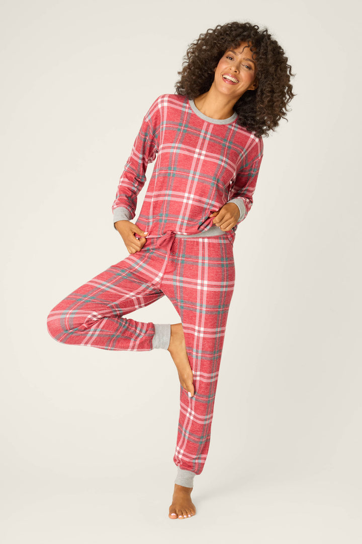 Wearing the P.J. Salvage Let's Get Toasty Red Plaid Pants Set, a person smiles on one leg with a hand in their pocket and the other on their hip, posed against a plain light background.