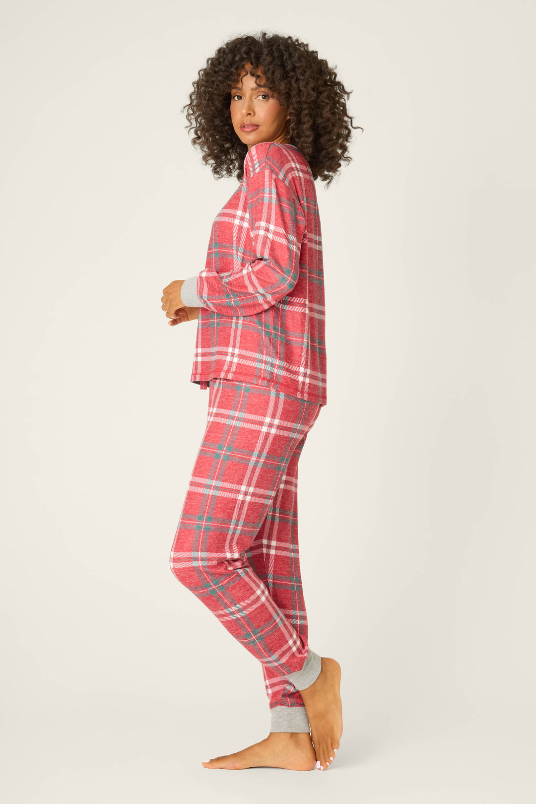 A person stands barefoot in profile on a light background, wearing the P.J. Salvage Let's Get Toasty Red Plaid Pants Set with gray cuffs.