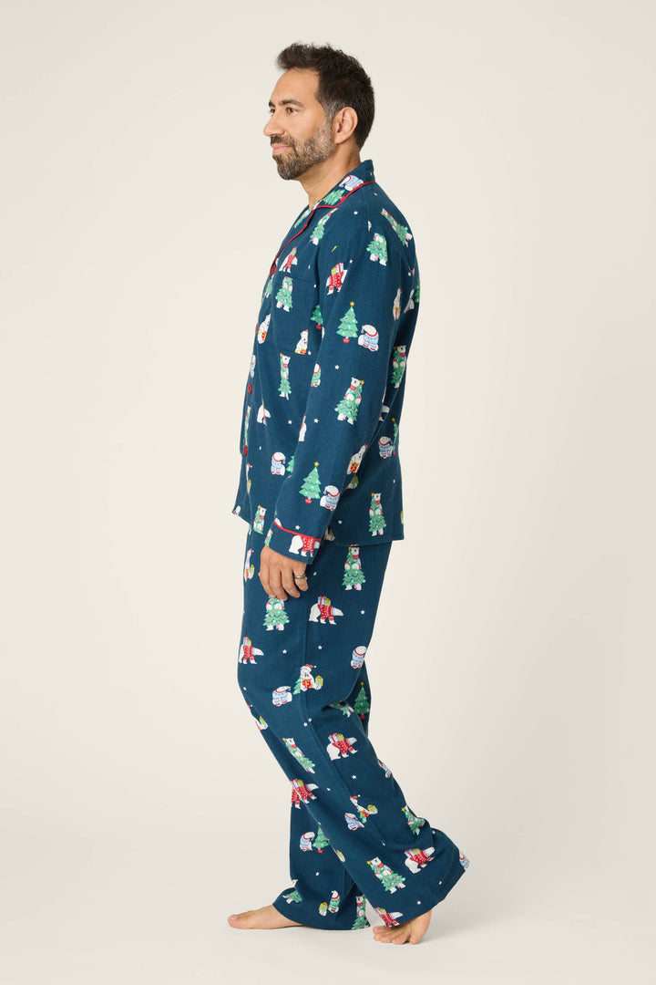 A man stands in profile barefoot against a plain light background, wearing the P.J. Salvage BEARS MENS PJ SET FAM JAM BEARLY AWAKE, a matching dark blue pajama set with colorful holiday prints.