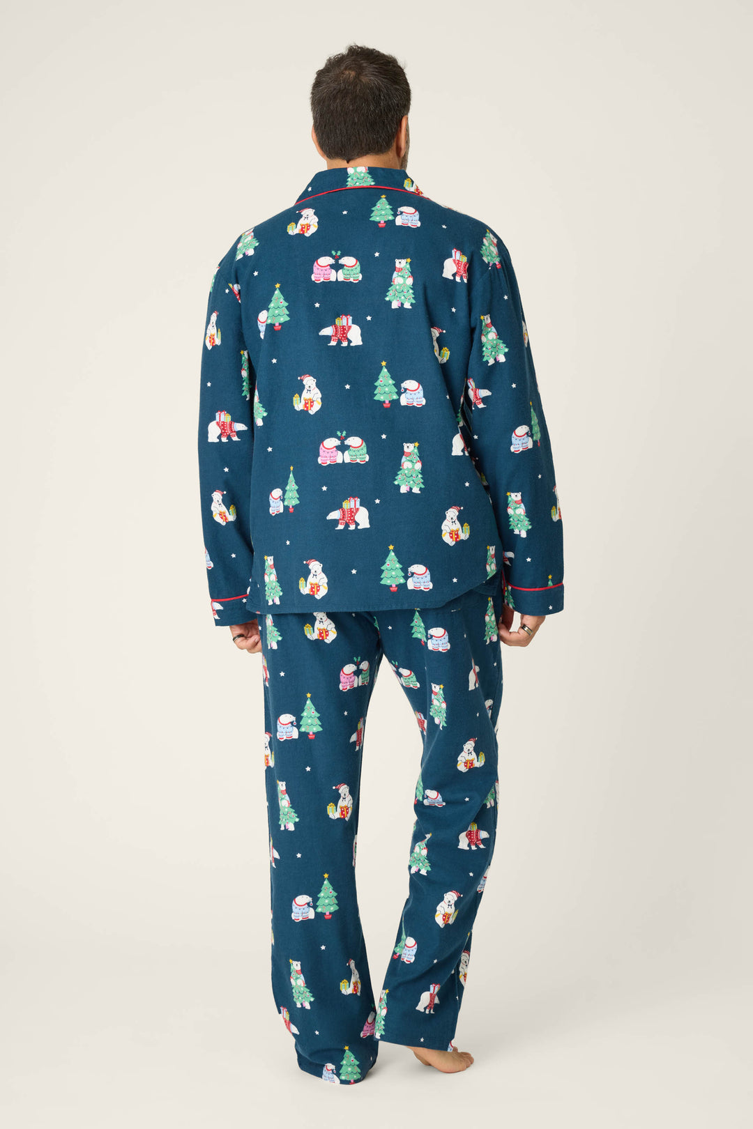 A person stands barefoot facing away in the BEARS MENS PJ SET FAM JAM BEARLY AWAKE by P.J. Salvage, featuring blue pajamas with festive bear prints, against a plain light background.