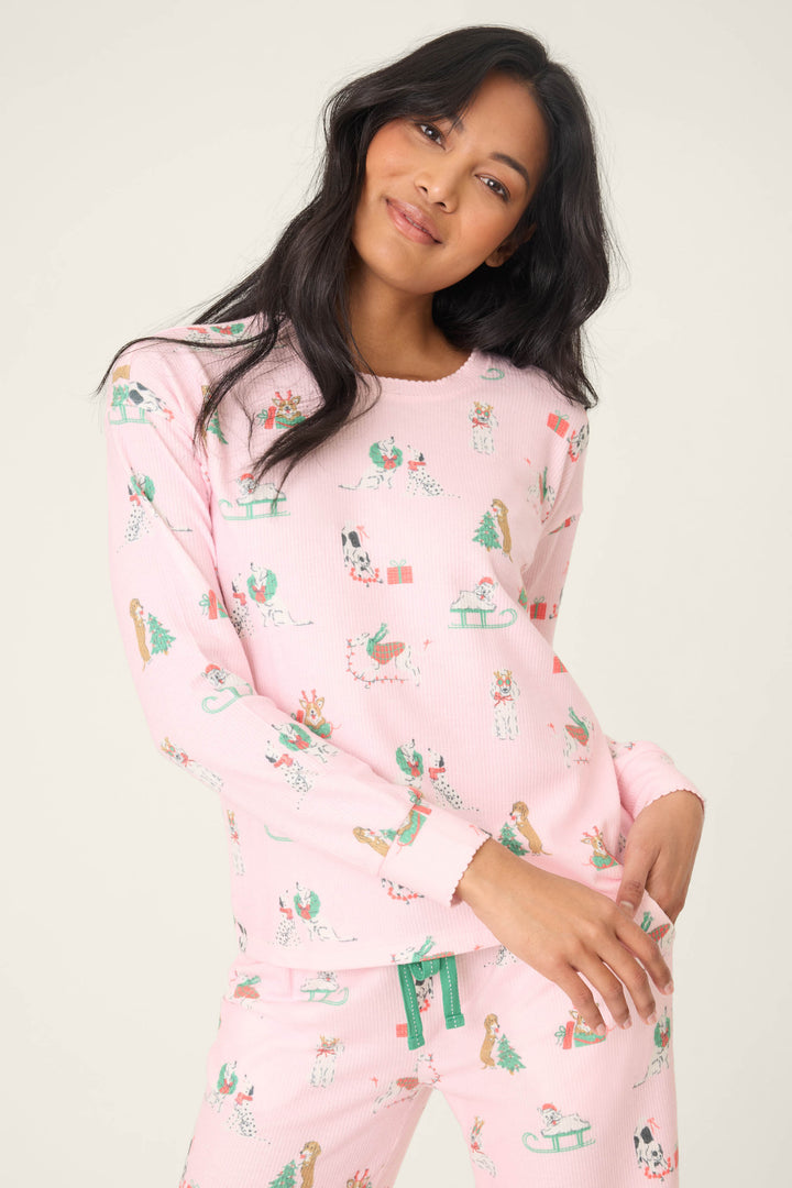 A woman with long dark hair wears the P.J. Salvage Peace & Pawlidays Dog Print Long Sleeve Top, standing against a plain light background, tilting her head and resting one hand on her hip.