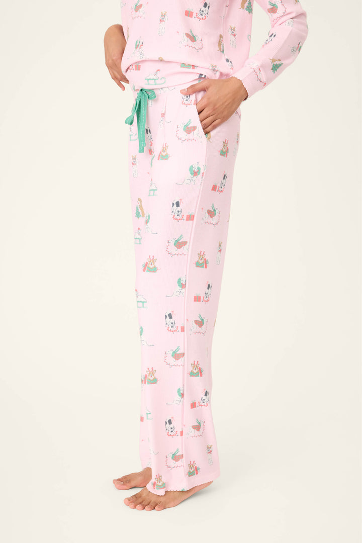 A person is shown from the waist down, barefoot against a plain background, wearing P.J. Salvage Peace & Pawlidays Dog Print Open Leg Pants with holiday-themed dog prints and a green drawstring.