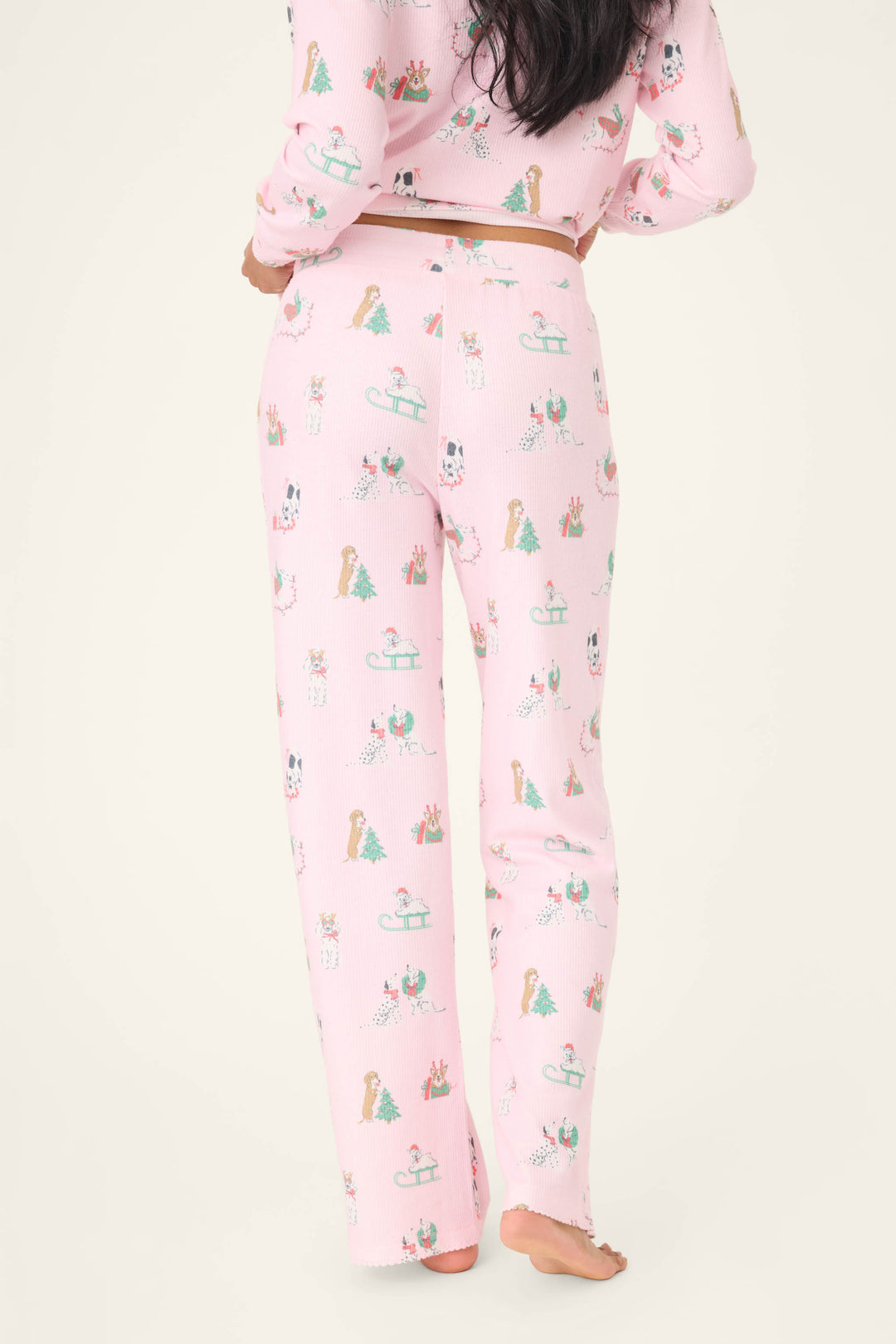 A person stands barefoot facing away, wearing P.J. Salvage Peace & Pawlidays Dog Print Open Leg Pants; only the lower back, legs, and part of the arms are visible.