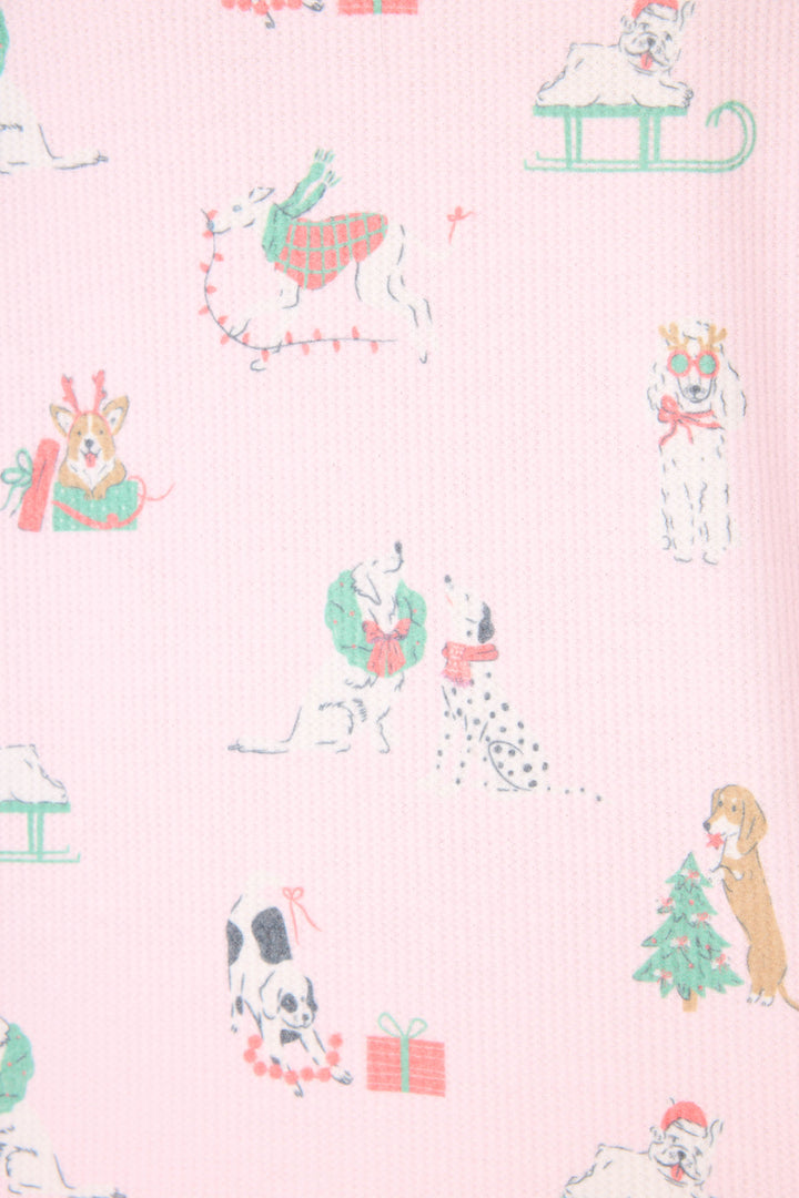 The P.J. Salvage Peace & Pawlidays Dog Print Pants Set features pink fabric decorated with festive dog illustrations, including pups in scarves, with wreaths, sledding, playing with lights, and a Christmas tree with a present.