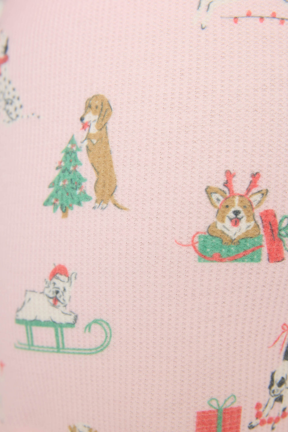 A close-up of P.J. Salvage’s DOGS SHORT PEACE & PAWLIDAYS shows light pink fabric with festive dog illustrations—wearing antlers, beside a Christmas tree, and riding a sleigh.