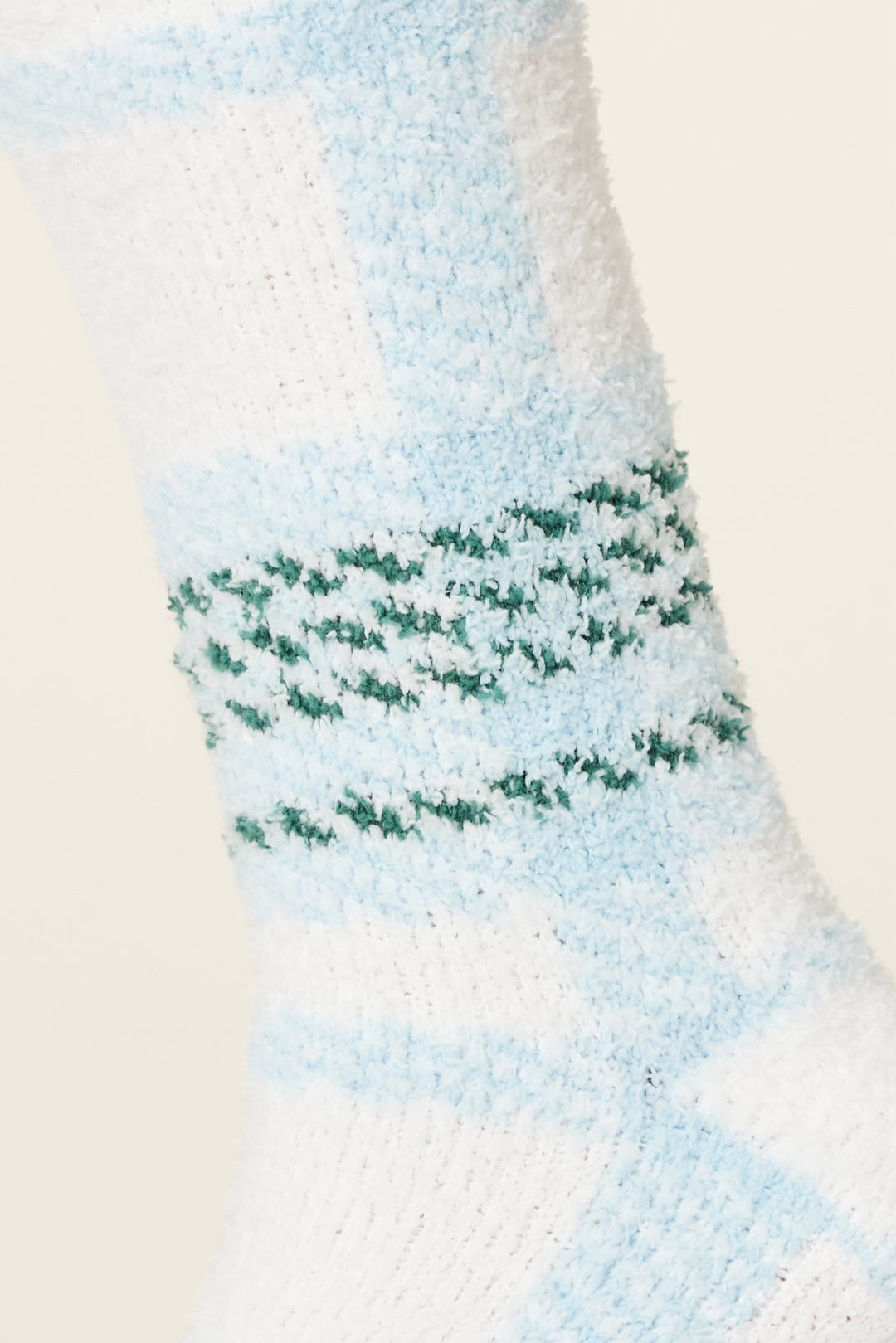 A close-up of P.J. Salvage Ski Jammie Plaid Crew Socks with Grippers, featuring a fuzzy white texture, light blue stripes, and three green dotted lines around the ankle for a cozy look.