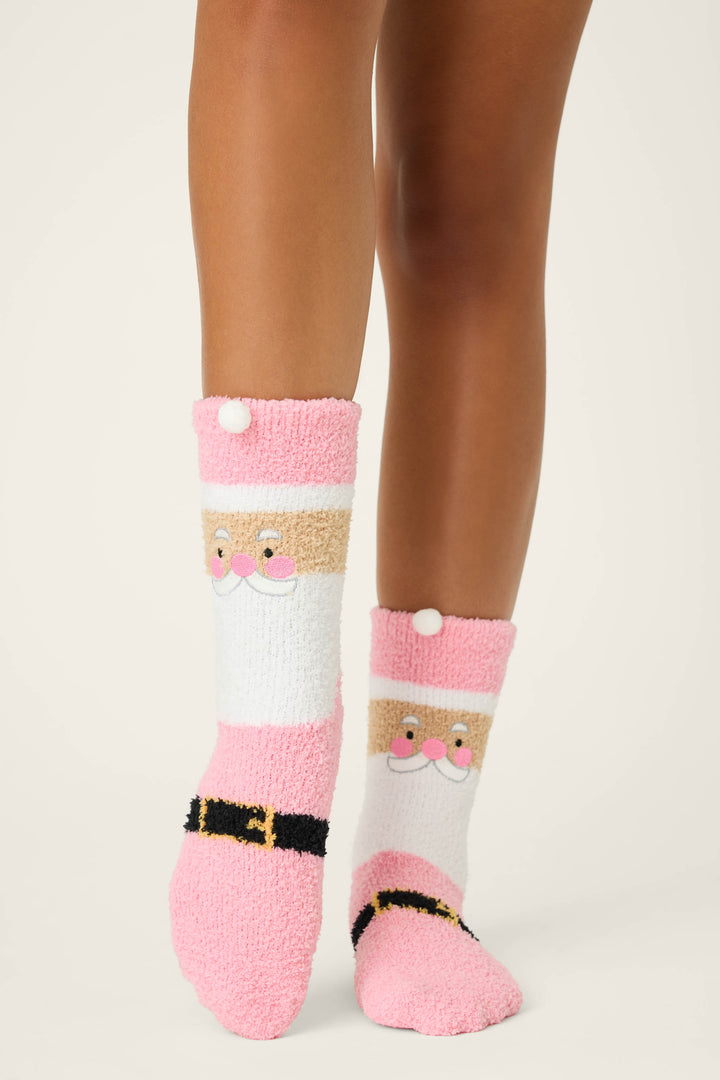 Someone wears P.J. Salvage SANTA SOCKS SKI JAMMIE CLASSICS, featuring fuzzy pink and white fabric with a Santa Claus face and black belt, standing on a light-colored surface.