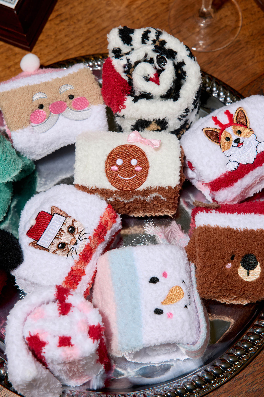 A silver tray displays several pairs of P.J. Salvage SANTA SOCKS SKI JAMMIE CLASSICS, each rolled up and featuring holiday designs like a snowman, gingerbread, corgi, cat in a Santa hat, polar bear, and festive patterns.