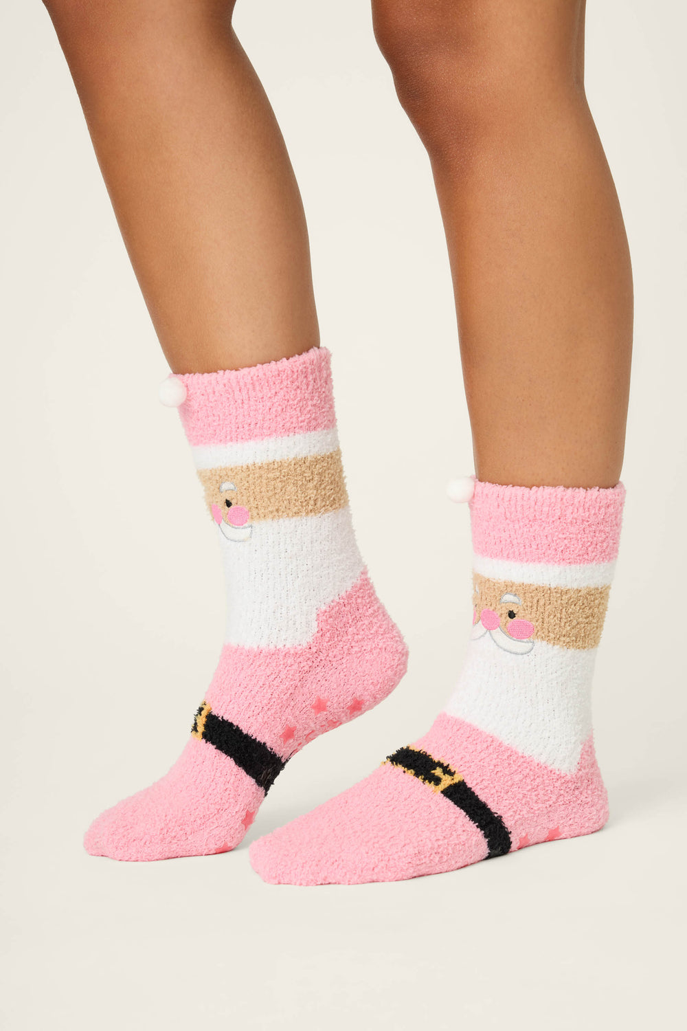 A person wears SANTA SOCKS SKI JAMMIE CLASSICS by P.J. Salvage—fluffy pink and white socks with a cartoon Santa face and black belt detail—against a plain background.