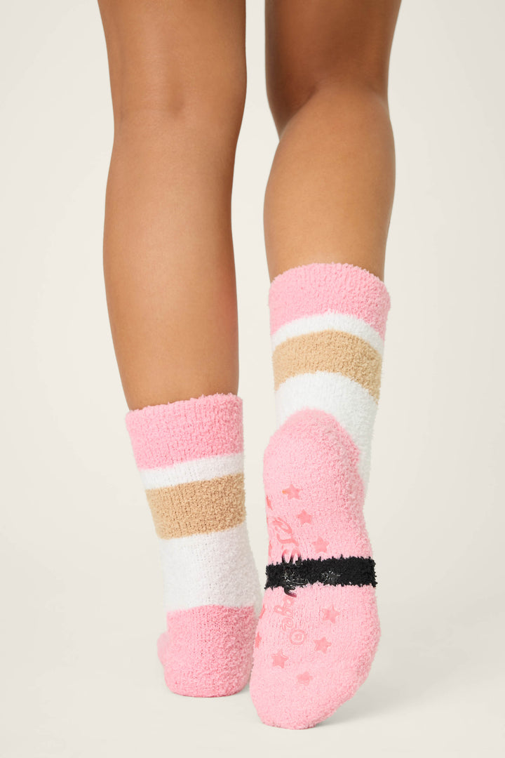 A person is wearing P.J. Salvage SANTA SOCKS SKI JAMMIE CLASSICS—fuzzy socks with pink, white, and beige stripes plus pink stars and a black non-slip grip band—shown from behind against a light background.