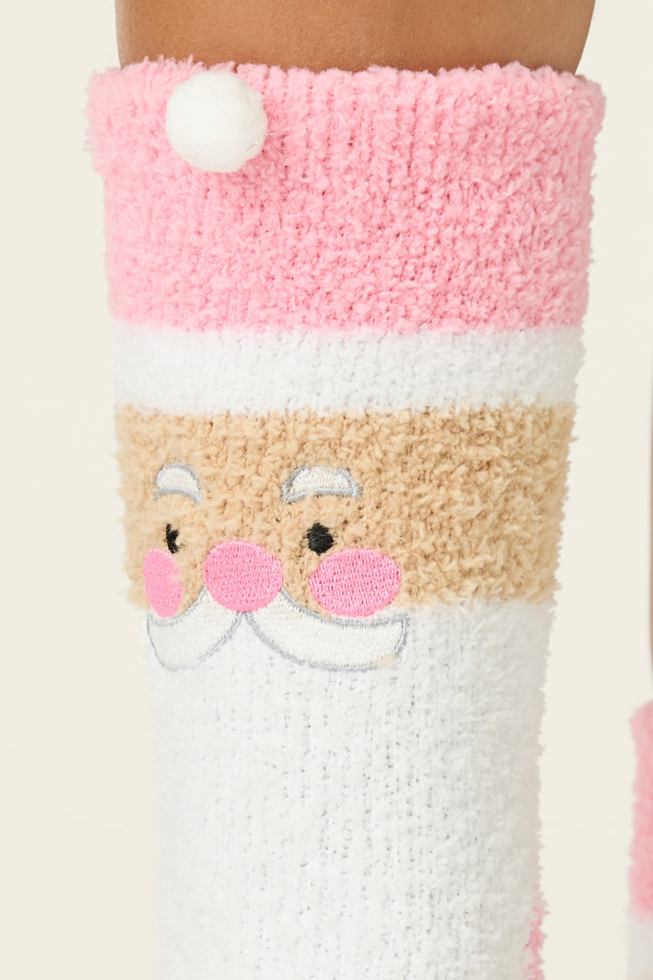 The P.J. Salvage Ski Jammie Classics Pink Santa Crew Socks with Grippers feature a smiling Santa face with a white mustache, pink cheeks, and a pom-pom accent in shades of pink, white, and beige.