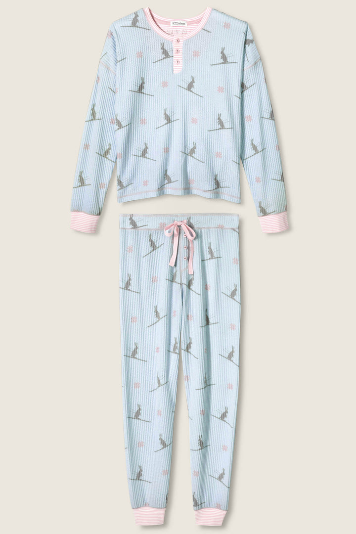 The P.J. Salvage Ski Jammie Classics Ski Bunny PJ Set is a two-piece pajama with light blue and white stripes, grey dinosaur silhouettes, pink dots, and light pink trim on the cuffs, neckline, and waistband.