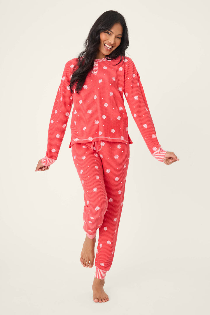 A woman smiles while standing barefoot on one leg, modeling the P.J. Salvage Ski Jammie Snowflake Print PJ Set against a plain light background.