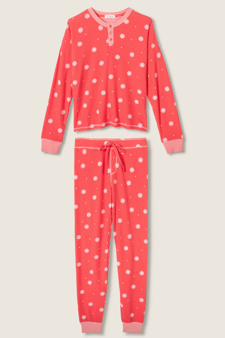 The P.J. Salvage Ski Jammie Snowflake Print PJ Set features a matching long-sleeve top with button neckline and long pants with drawstring waist and cuffed ankles, all adorned with a charming red snowflake print.