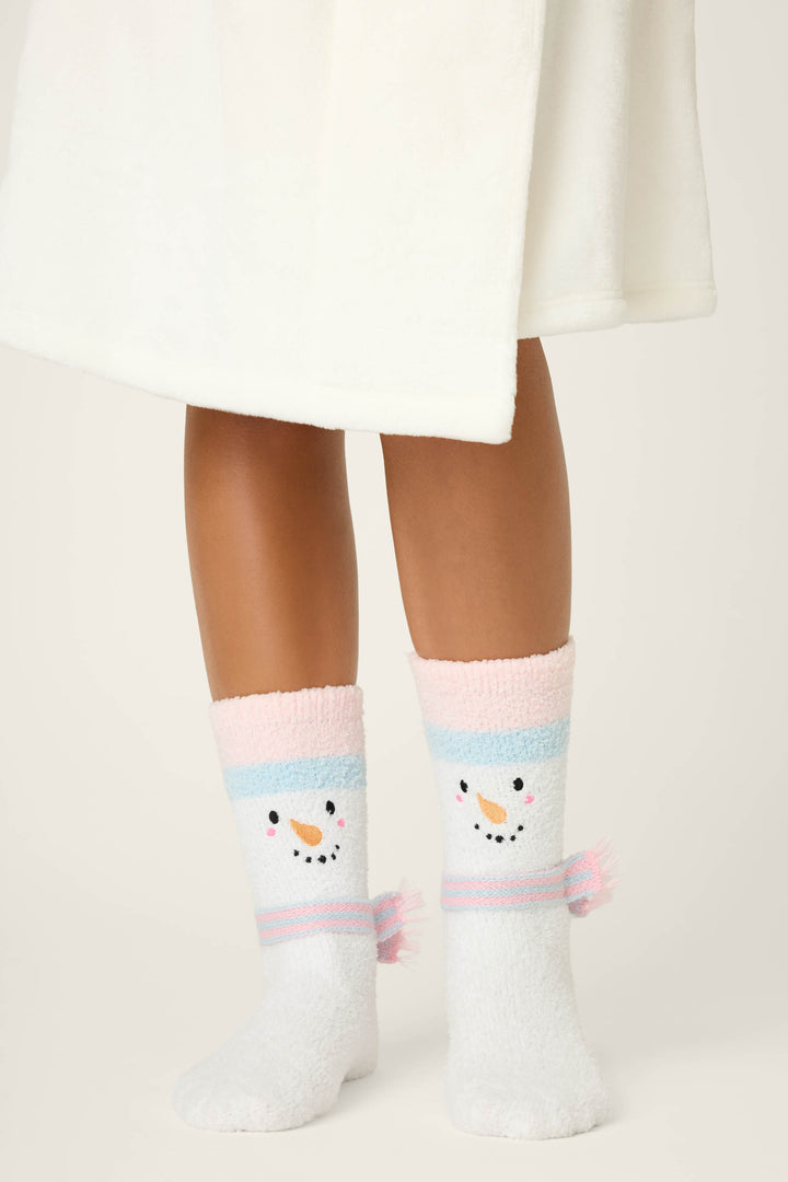 A person in a white robe stands on a light surface, wearing P.J. Salvage SNOWMAN SOCKS SKI JAMMIE CLASSICS featuring fuzzy white fabric, pastel pink and blue stripes, and snowman faces on the front.
