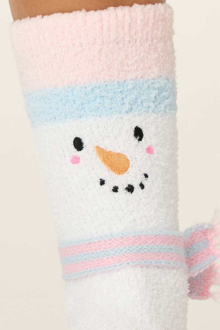 A close-up of P.J. Salvage Ski Jammie Classics Snowman Crew Socks with Grippers, featuring a fuzzy white finish, snowman face with pink cheeks, carrot nose, black dotted smile, and pastel pink/blue striped accents.