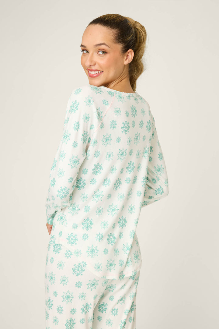 A woman with light brown hair in a ponytail smiles at the camera, wearing the P.J. Salvage Snowflake Wishes Pointelle Henley Top—white sleepwear with a light blue snowflake pattern—against a plain background.