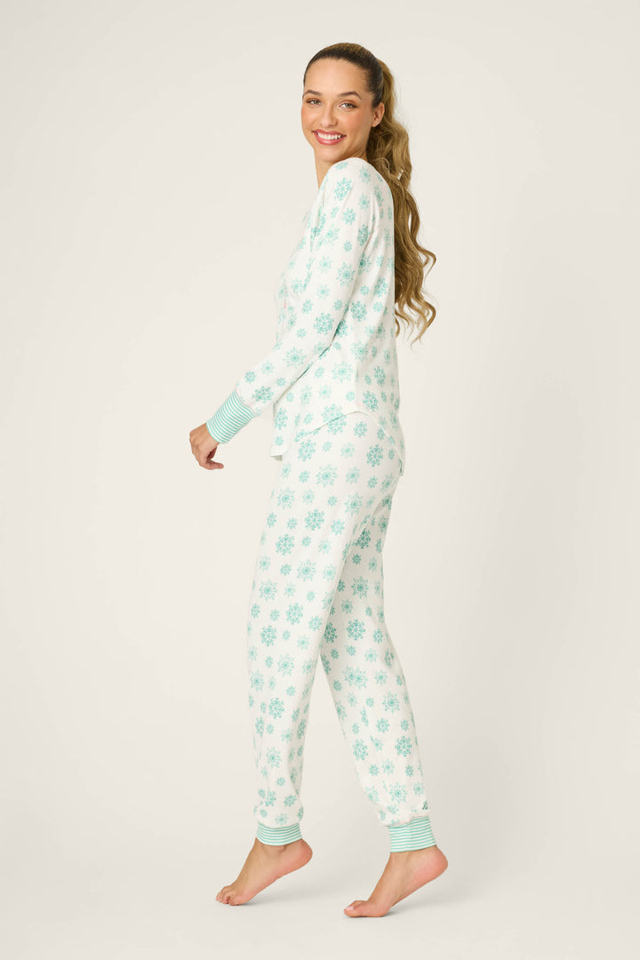 A person stands barefoot on one foot, smiling over their shoulder in the Snowflake Wishes Pointelle Pants Set by P.J. Salvage, featuring a blue snowflake pattern, against a plain background.