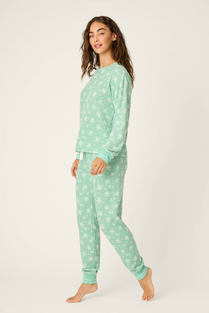 A person stands barefoot, slightly turned, against a plain light background, wearing the P.J. Salvage DTC Exclusive - SNOWFLAKE PJ SET 3 PIECE GIFT SET in mint green with a white snowflake pattern.