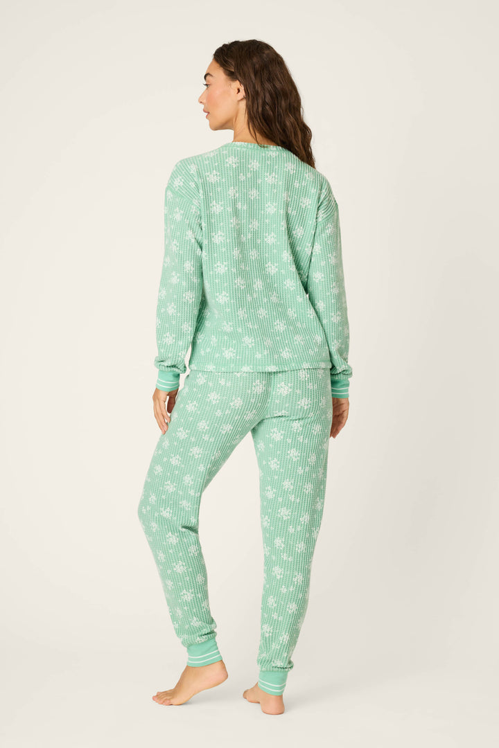 A woman stands barefoot against a plain background, facing away, wearing the P.J. Salvage DTC Exclusive SNOWFLAKE PJ SET 3 PIECE GIFT SET in mint green with a white cactus pattern.