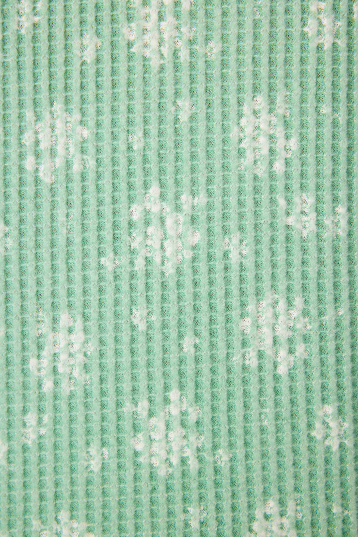 Close-up of the P.J. Salvage DTC Exclusive - SNOWFLAKE PJ SET 3 PIECE GIFT SET featuring textured green fabric with a vertical ribbed pattern and scattered white snowflake designs.