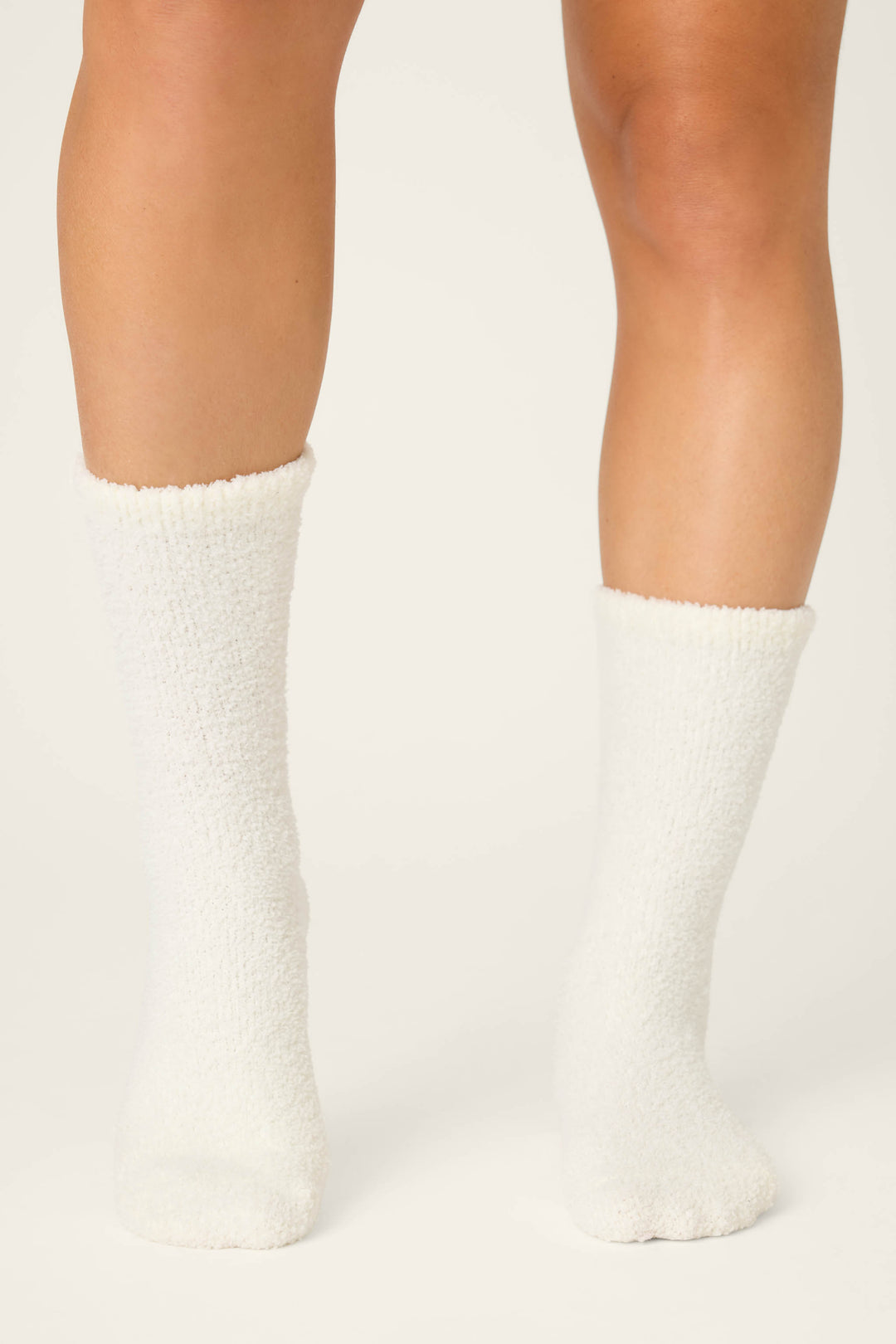 A person wearing P.J. Salvage's DRINK SOCKS LET'S GET TOASTY in white, fuzzy style stands on a neutral background, with only their lower legs and feet visible.