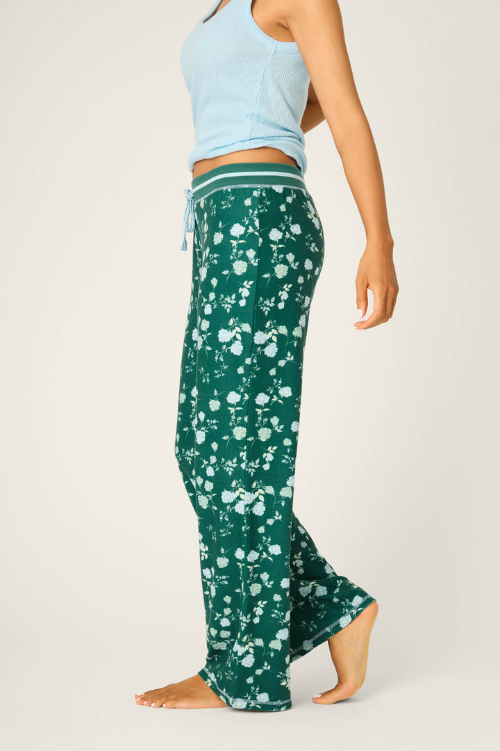 A person in a light blue sleeveless top and P.J. Salvage Winter Wonderland Floral Thermal Velour Open Leg Pants stands barefoot on a light background, shown from the side with their right arm down and left arm slightly bent.