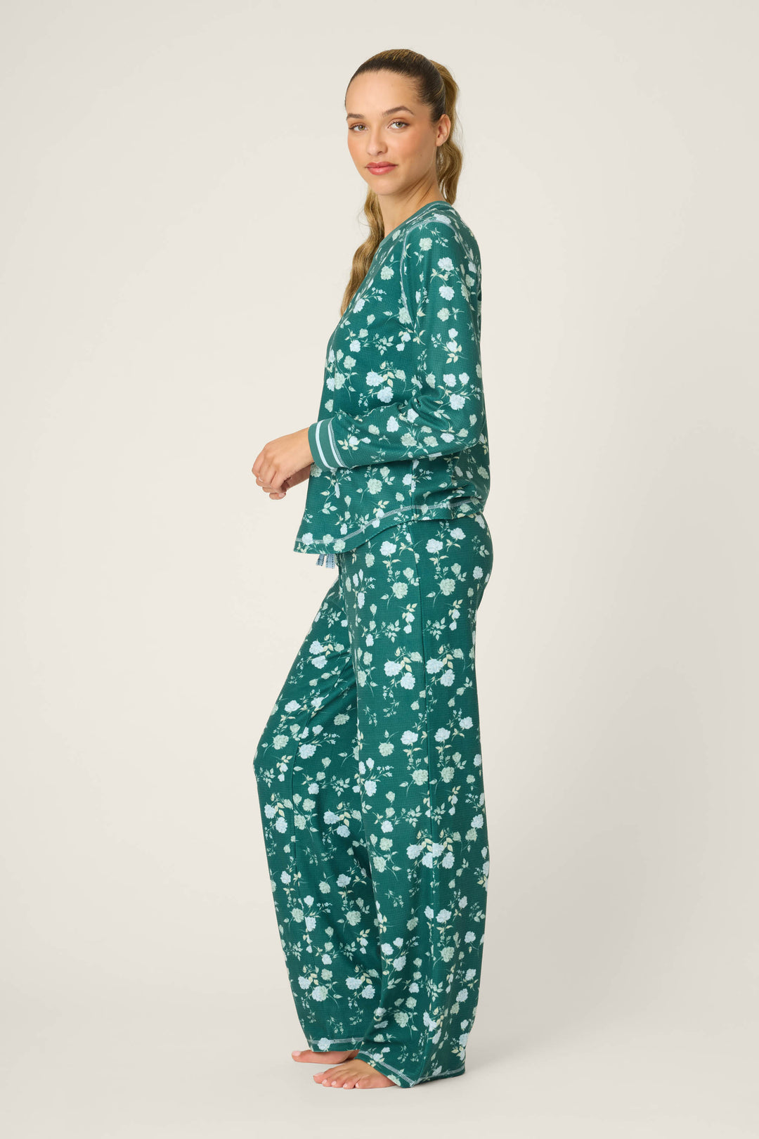 A woman stands barefoot on a plain background, wearing the P.J. Salvage FLORAL PJ SET WNTER LAND in teal with a white floral pattern. She faces sideways, turning her head slightly toward the camera.