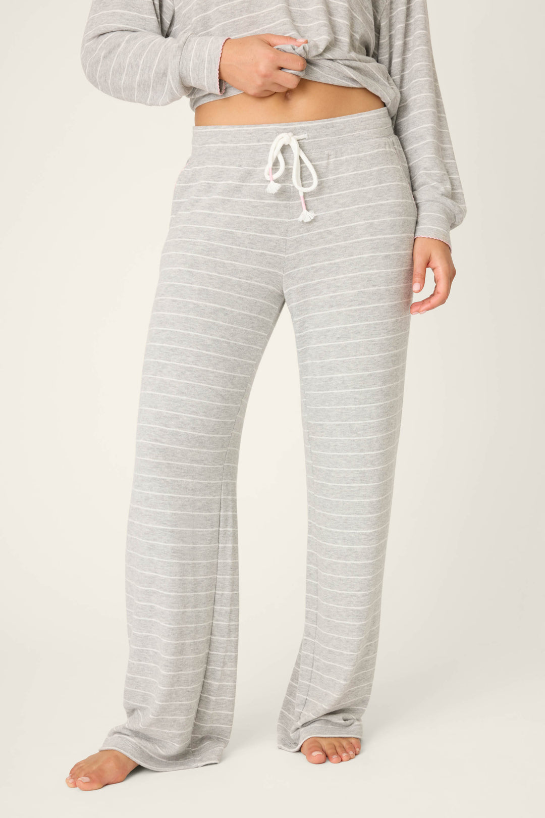 A person models P.J. Salvage's My Dog Is My Valentine Striped Open Leg Pants in light gray with a white drawstring, standing barefoot on a light background. The matching long-sleeve top is partially visible.