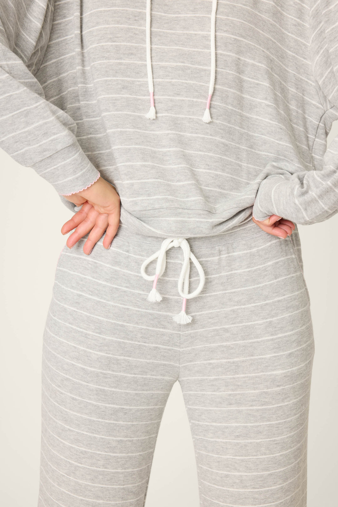 Someone wearing P.J. Salvage's "My Dog Is My Valentine Striped Open Leg Pants"—a light gray, long-sleeve, hooded top, and matching drawstring pants with thin white stripes—stands stylishly with one hand on their hip.