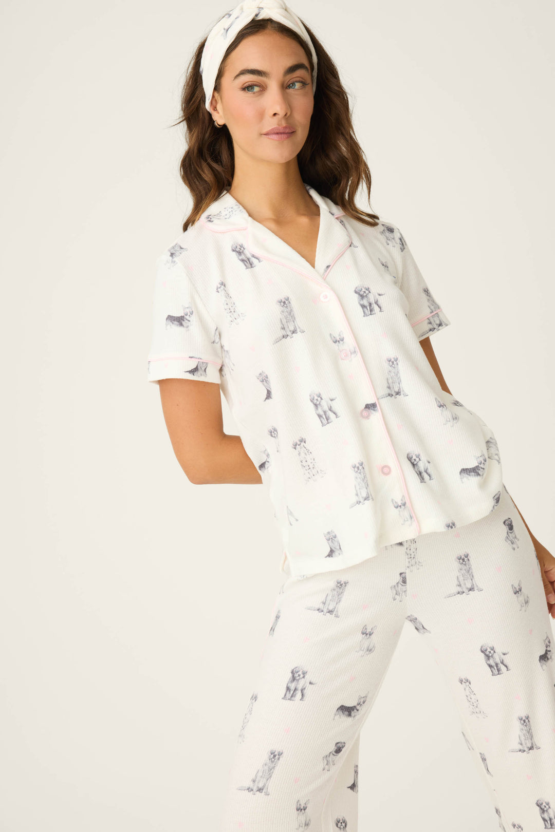 A woman wears the P.J. Salvage "My Dog Is My Valentine" 3-piece PJ set—white with a dog print and paired with a matching headband—standing against a plain background, hand in pocket and expression neutral.