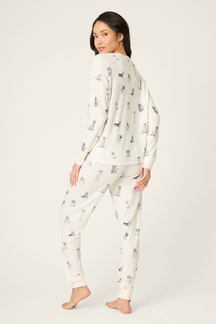 A woman stands barefoot on a light background, wearing the P.J. Salvage My Dog Is My Valentine PJ Set. She is turned partly to the side, looking over her shoulder with her left hand on her hip.