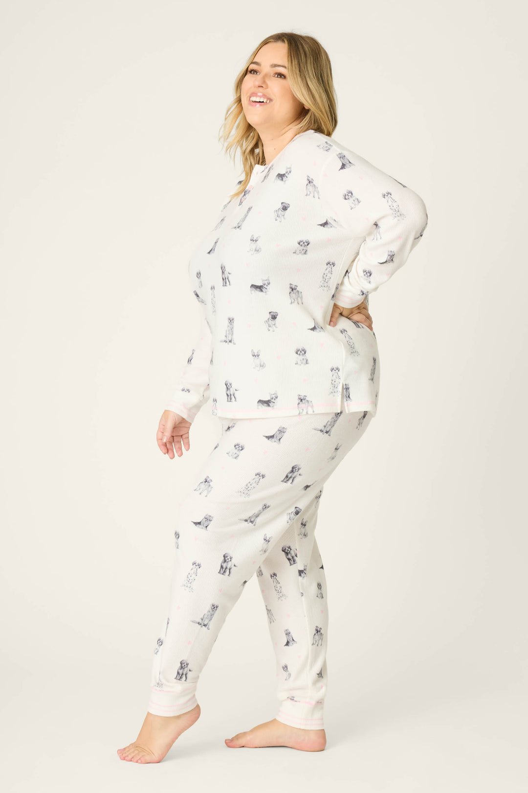 A person poses barefoot on a plain background, smiling and relaxed, wearing the P.J. Salvage "My Dog Is My Valentine" Plus Size PJ Set featuring a subtle animal print.