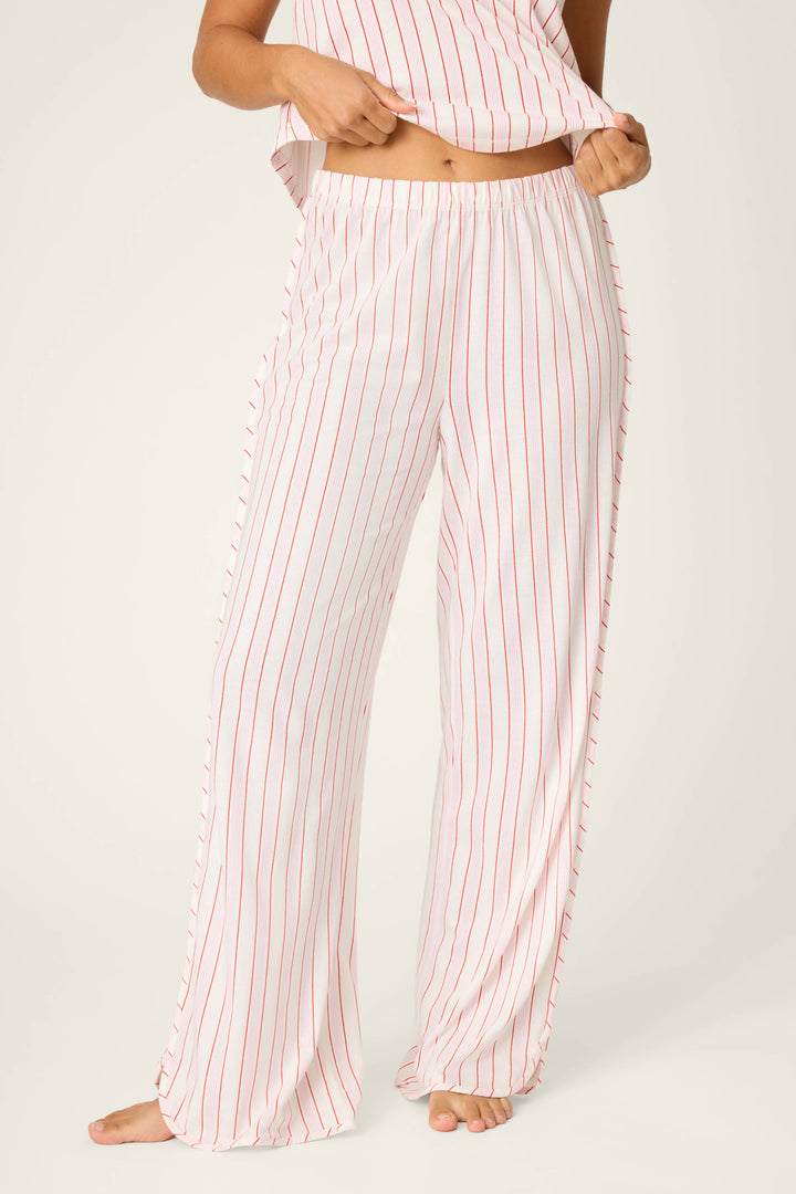 A person stands barefoot in P.J. Salvage's Feeling Loved Striped Open Leg Pants, featuring comfy cotton-modal fabric with red vertical stripes, holding up part of a matching top to show their midriff against a light plain background.