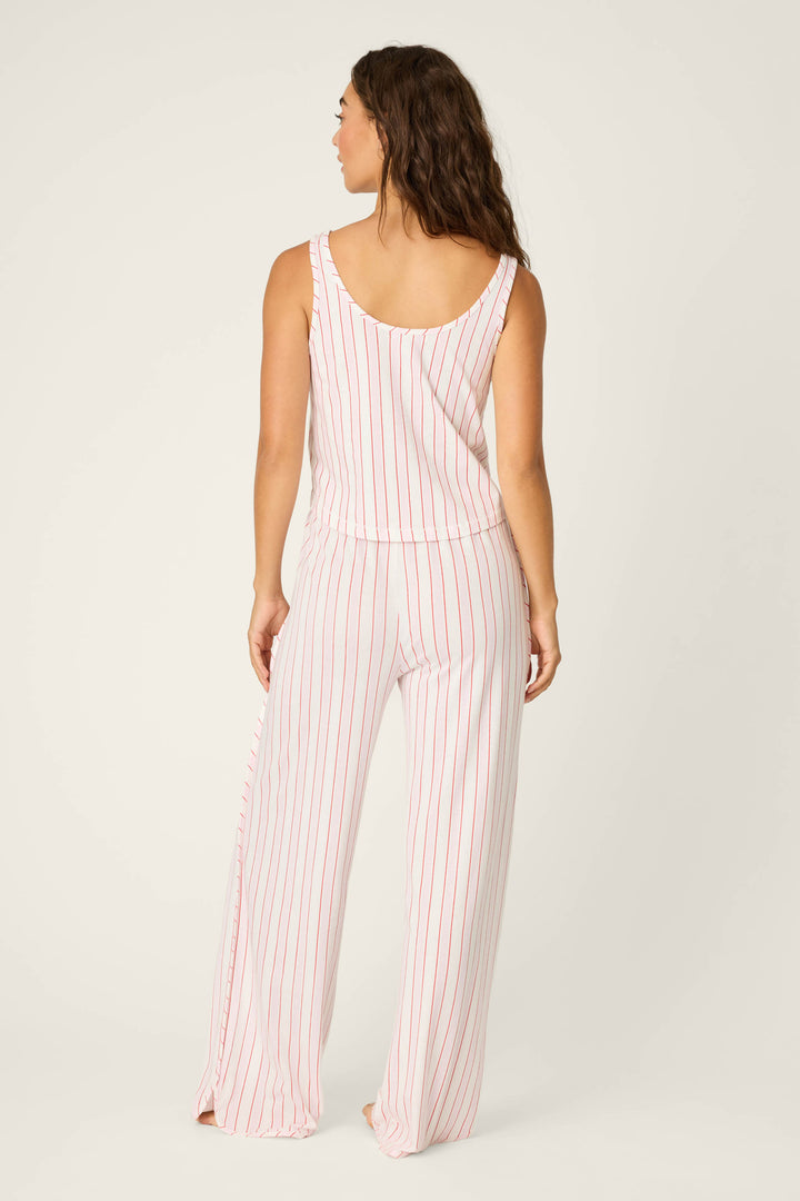 A woman with long wavy hair stands with her back to the camera, wearing the P.J. Salvage Feeling Loved Striped PJ Set— a sleeveless top and wide-leg pants with vertical red stripes on white—against a plain light background.