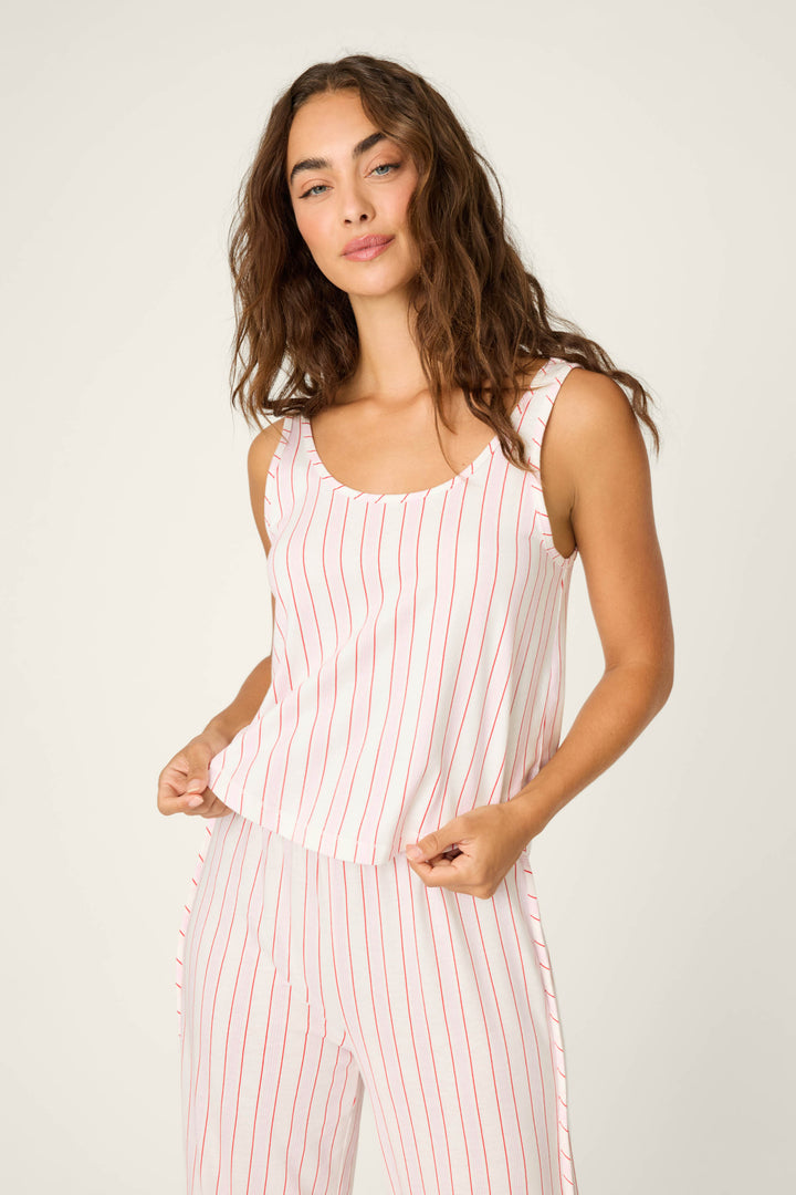 A woman with long, wavy brown hair wears the P.J. Salvage Feeling Loved Striped Tank Top—a relaxed fit, sleeveless white pajama top with red vertical stripes—standing against a plain background and looking at the camera neutrally.