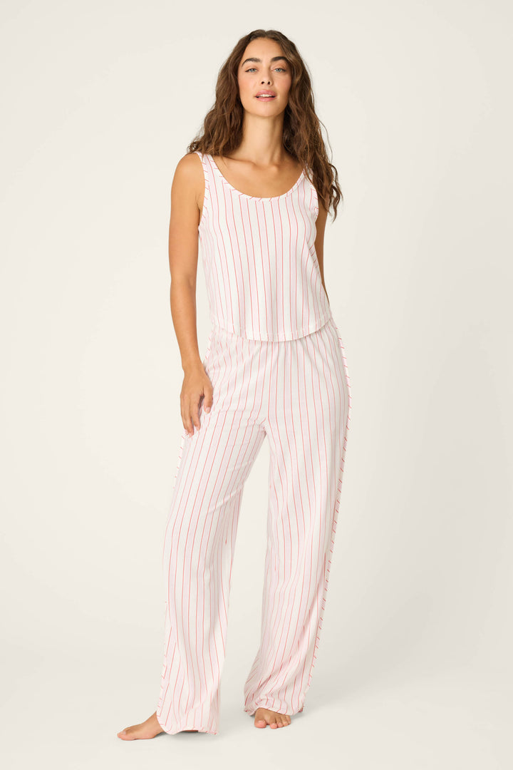 A woman with long, wavy brown hair stands barefoot against a plain background, wearing the P.J. Salvage Feeling Loved Striped Tank Top—a relaxed fit with white and light red vertical stripes for a laid-back look.