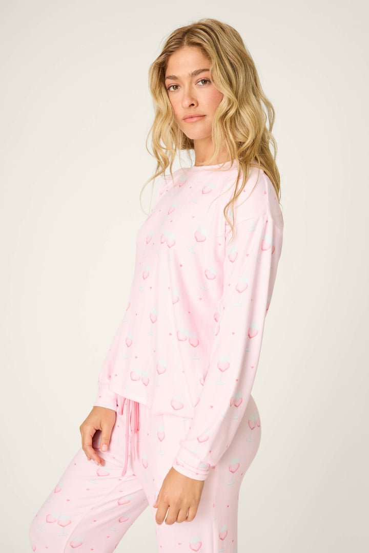 A woman with long blonde hair wears the P.J. Salvage Happy Hour Wine Glass Print Long Sleeve Top, standing against an off-white background and looking at the camera.