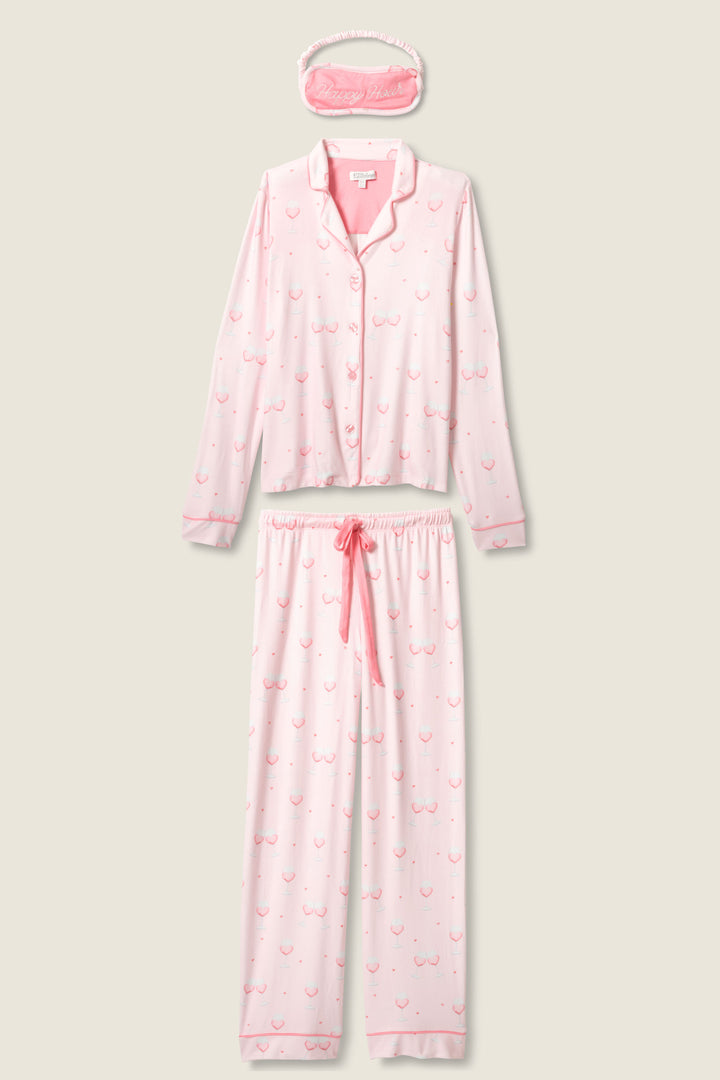 The P.J. Salvage Happy Hour Wine Glass Print 3-Piece PJ Set features a pink button-up long-sleeve top, matching drawstring pants, and a sleep mask with an outlined wine glass pattern.