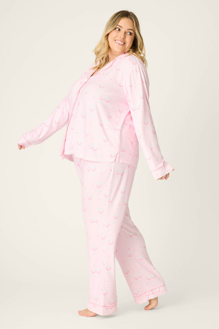 A woman models the P.J. Salvage Happy Hour Wine Glass Print 3-Piece Plus Size PJ Set, standing barefoot against a plain background with a smile, looking over her shoulder and extending one arm slightly to the side.